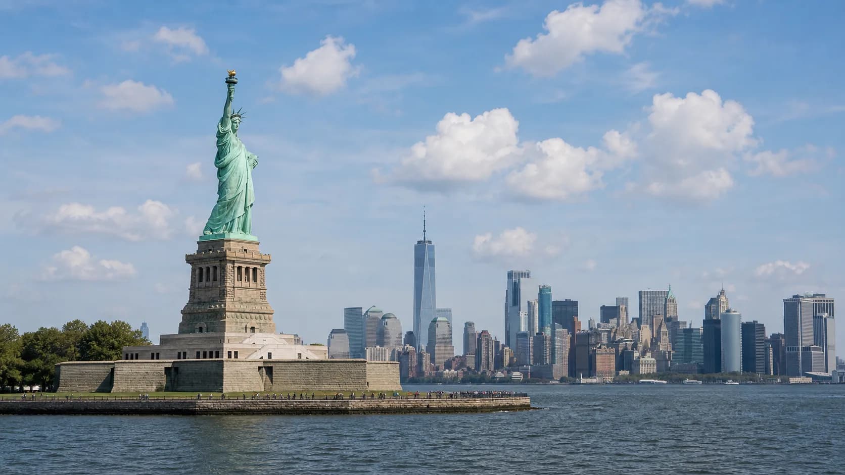 The Statue of Liberty stands on her island with the Manhattan skyline across the water behind her.